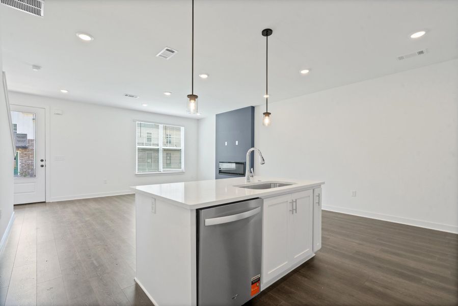 Modern kitchen island with a built-in stainless steel dishwasher, undermount sink, and pendant lighting