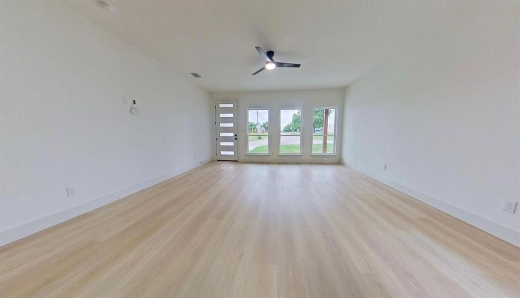Spacious room featuring wood-finish flooring, white baseboards, and a modern ceiling fan