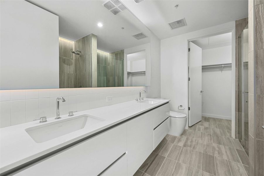The primary bathroom showcases a dual vanity with sleek white cabinets, providing ample storage & a modern aesthetic plus a large horizontal mirror, enhancing the spacious feel and functionality of the area. The primary bathroom showcases a dual vanity with sleek white cabinets, providing ample storage & a modern aesthetic plus a large horizontal mirror, enhancing the spacious feel and functionality of the area.
