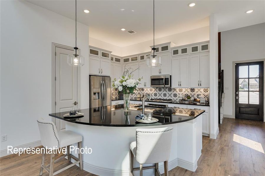 Kitchen featuring hanging light fixtures, backsplash, stainless steel appliances, hardwood / wood-style flooring, and an island with sink