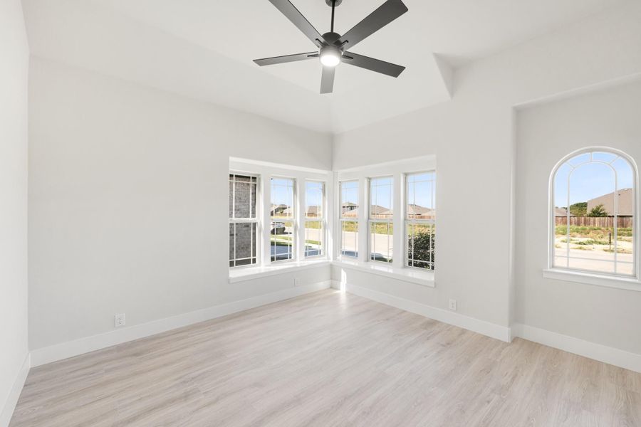 Empty room with light wood floors, ceiling fan, corner windows, and an arched window with natural light