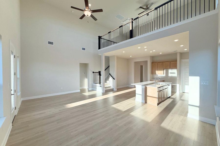 Unfurnished living room with a ceiling fan, light wood-style flooring, a towering ceiling, recessed lighting, and stairway