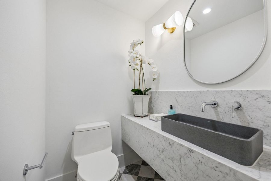 Second Powder Room located next to MUD Area to service the Back Covered Lanai with a 24 x 24 Checkerboard Matte Porcelain Tile in Calcutta and Amani Grey. Floating Slab Quartz Counter and Backsplash, Rectangular Concrete Vessel Sink, Wall Mounted Widespread Bathroom Faucet in Polished Chrome, Oval Mirror and a White Striped Glass Sconce. Second Powder Room located next to MUD Area to service the Back Covered Lanai with a 24 x 24 Checkerboard Matte Porcelain Tile in Calcutta and Amani Grey. Floating Slab Quartz Counter and Backsplash, Rectangular Concrete Vessel Sink, Wall Mounted Widespread Bathroom Faucet in Polished Chrome, Oval Mirror and a White Striped Glass Sconce.