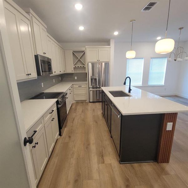 Kitchen featuring stainless steel appliances, tasteful backsplash, an island with sink, light wood-type flooring, and sink