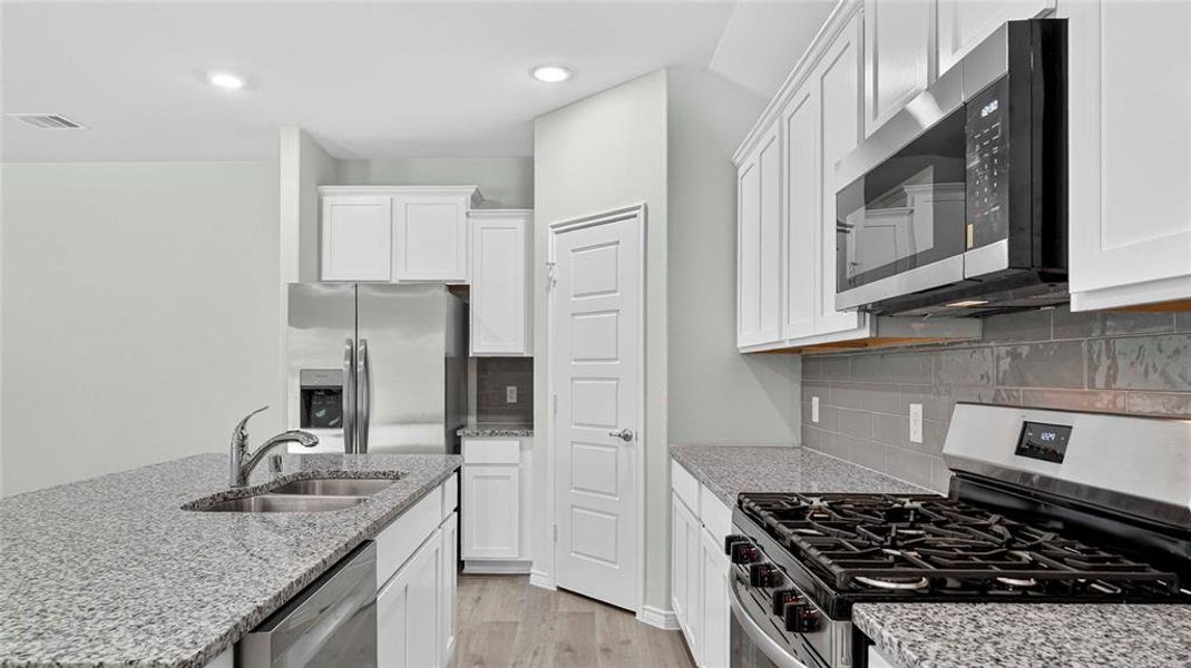 Kitchen featuring white cabinetry, granite countertops, stainless steel appliances, a gas range, and a subway tile backsplash