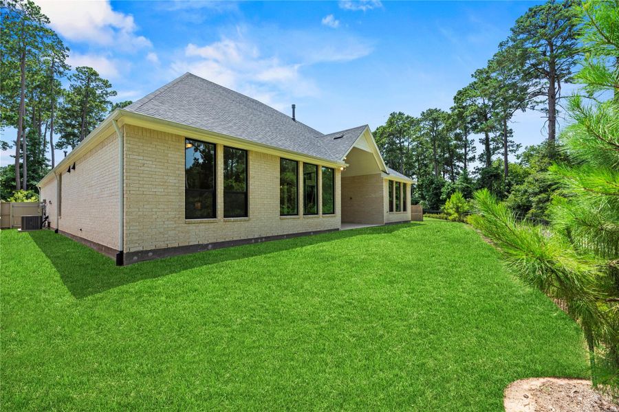The backyard offers lush greenery, a peaceful tree-lined backdrop, and a covered patio.