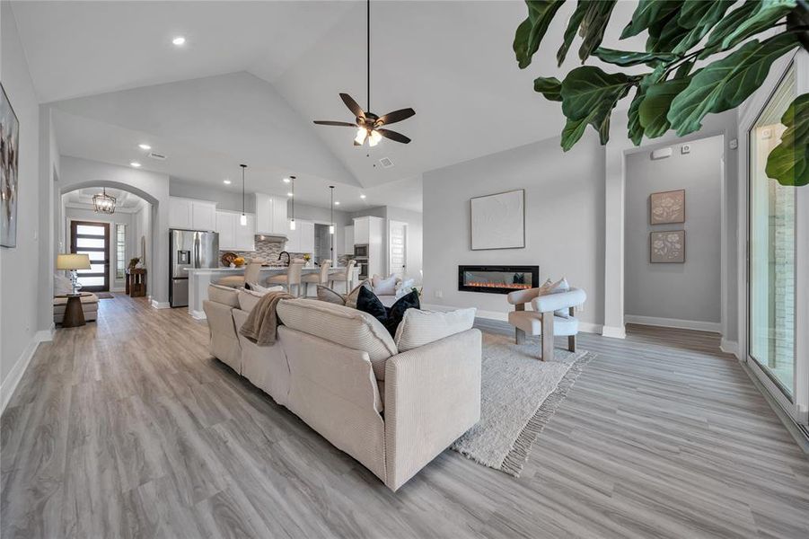 Living room featuring light wood-style flooring, high vaulted ceiling, a ceiling fan, arched walkways, and a glass covered fireplace Living room featuring light wood-style flooring, high vaulted ceiling, a ceiling fan, arched walkways, and a glass covered fireplace