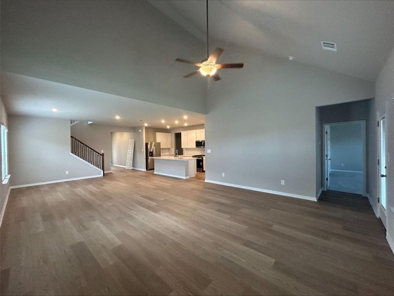 Unfurnished living room featuring wood finished floors, stairs, ceiling fan, recessed lighting, and high vaulted ceiling Unfurnished living room featuring wood finished floors, stairs, ceiling fan, recessed lighting, and high vaulted ceiling