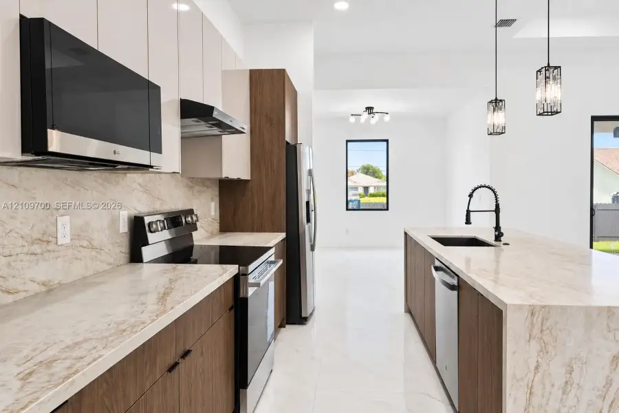Kitchen featuring stone-patterned countertops and backsplash, dual-tone cabinetry, stainless steel appliances, large center island with an undermount sink, and polished tile flooring
