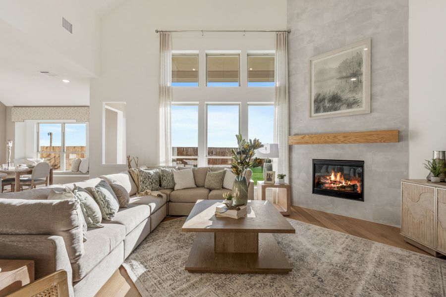 Living room with high ceilings, sectional sofa, wood-mantel fireplace, and large windows with natural light