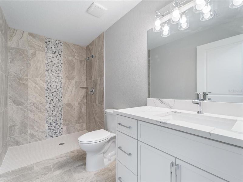 Guest bathroom boasts a fully tiled shower with zero edge entrance, solid wood cabinetry, and quartz countertop.