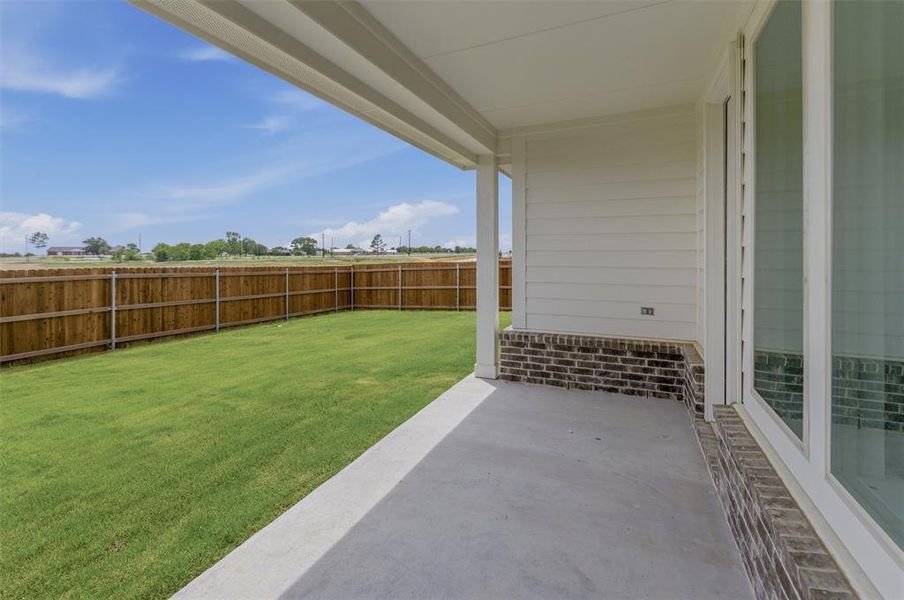 Rear patio with concrete flooring, covered ceiling, and dark brick wainscoting