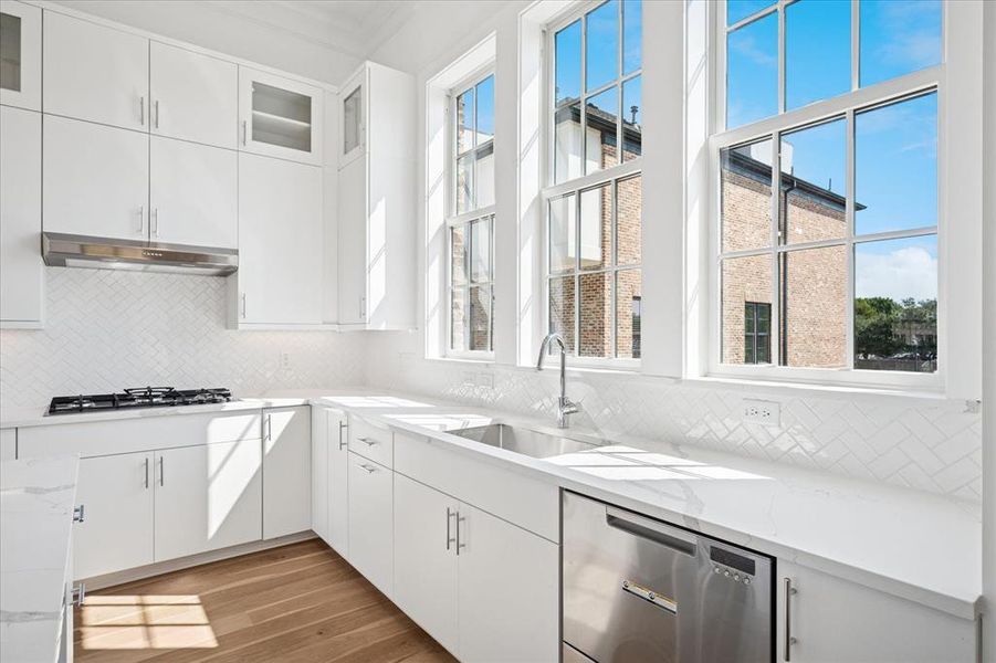 Kitchen with white cabinets, glass insert cabinets, dark wood finished floors, tasteful backsplash, and stainless steel dishwasher Kitchen with white cabinets, glass insert cabinets, dark wood finished floors, tasteful backsplash, and stainless steel dishwasher