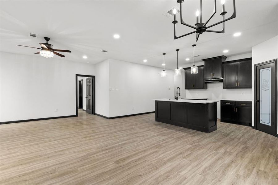 Kitchen with pendant lighting, ceiling fan with notable chandelier, sink, light wood-type flooring, and an island with sink