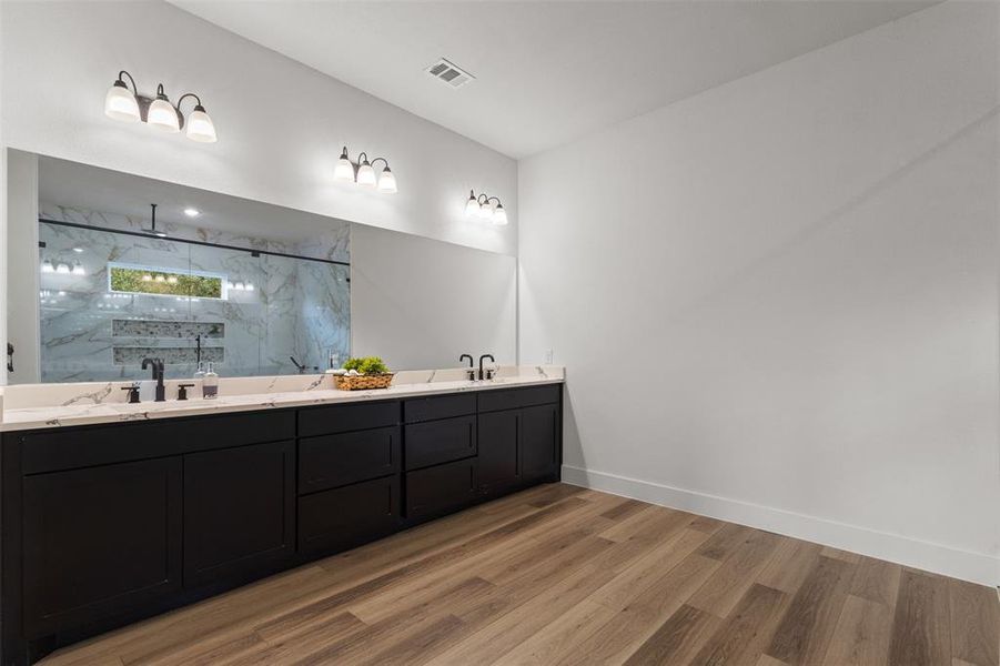 Full bathroom with a marble finish shower, double vanity, and light wood finished floors
