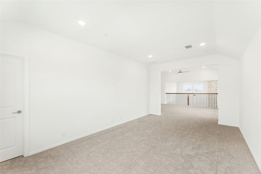 Spacious empty upstairs bonus room with beige carpet, white walls, recessed lighting, and open railing overlooking lower level.
