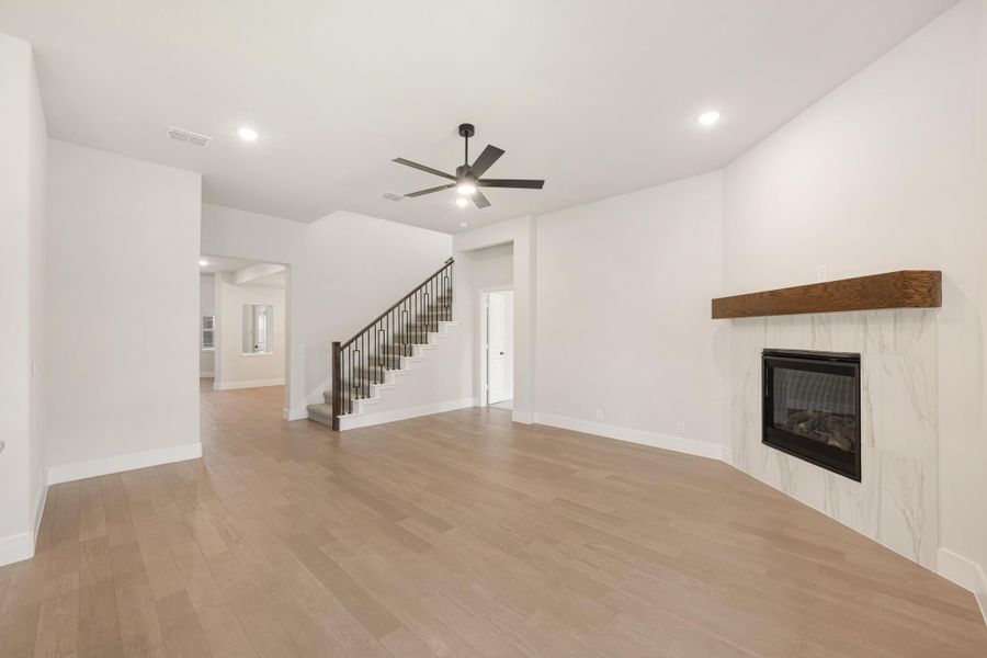 Open living room with hardwood floors, marble fireplace with wood mantel, ceiling fan, and staircase.