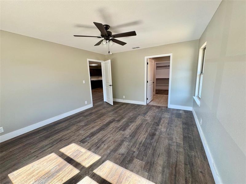 Unfurnished bedroom with a spacious closet, dark wood finished floors, and ceiling fan