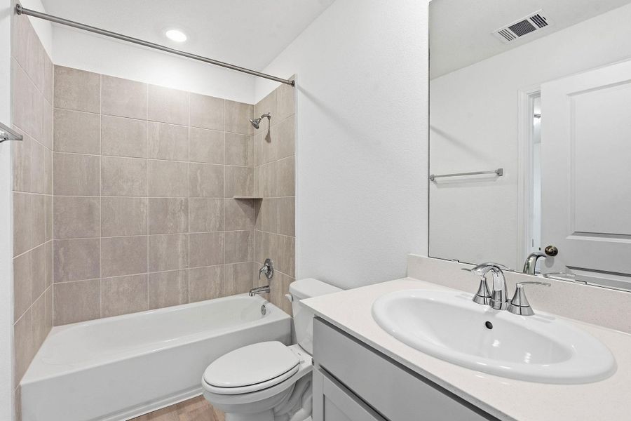 Bathroom featuring a white vanity with an undermount sink, a large mirror, and a tub-shower combination with light brown wall tiling and a built-in shelf Bathroom featuring a white vanity with an undermount sink, a large mirror, and a tub-shower combination with light brown wall tiling and a built-in shelf