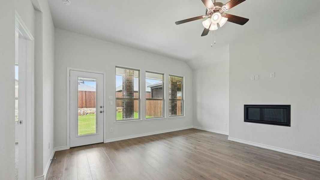 Spacious living area featuring wood-finish flooring, a contemporary fireplace insert, vaulted ceilings, and a ceiling fan with integrated lighting