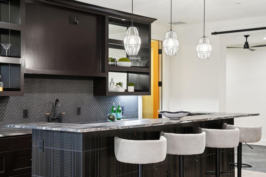 Kitchen in Basement featuring a kitchen bar, visible vents, decorative light fixtures, backsplash, and dark cabinetry