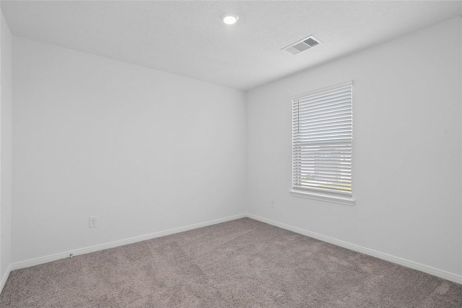 Bright and versatile secondary bedroom featuring plush neutral carpeting, clean tone-on-tone walls, and a large window with fitted blinds.