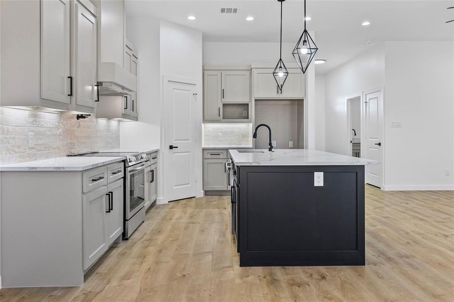 Kitchen featuring visible vents, a sink, light wood-type flooring, electric range, and a kitchen island with sink