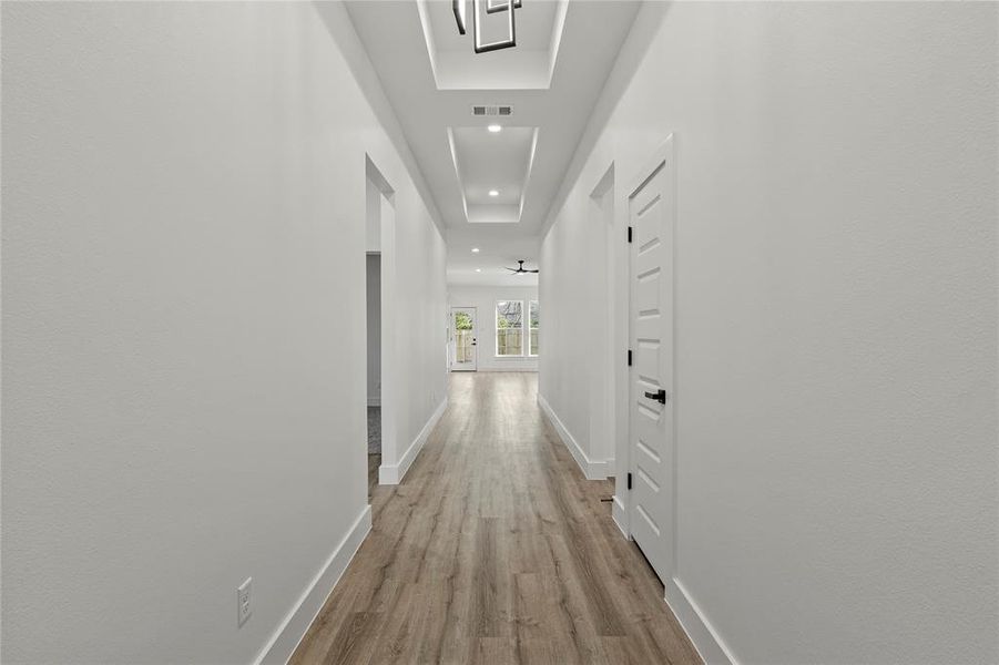 Corridor with a tray ceiling and light hardwood / wood-style flooring