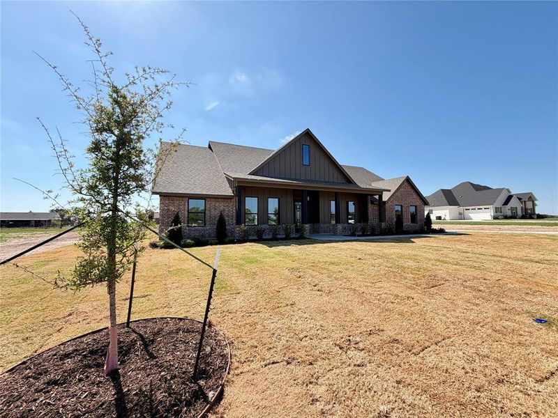 View of front facade with board and batten siding, covered porch, a front yard, and brick siding View of front facade with board and batten siding, covered porch, a front yard, and brick siding
