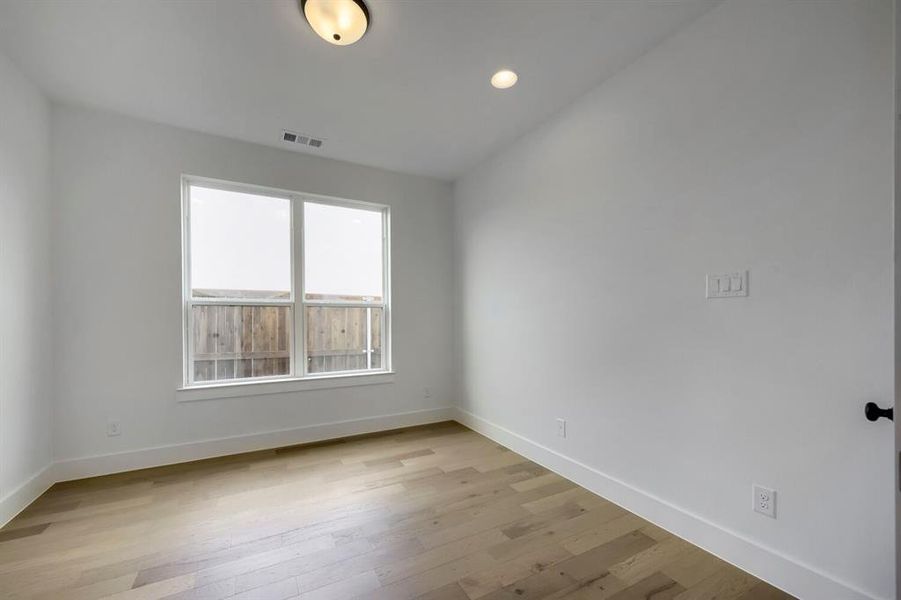 Room featuring wood-finish flooring, white walls, and a large window with white trim Room featuring wood-finish flooring, white walls, and a large window with white trim