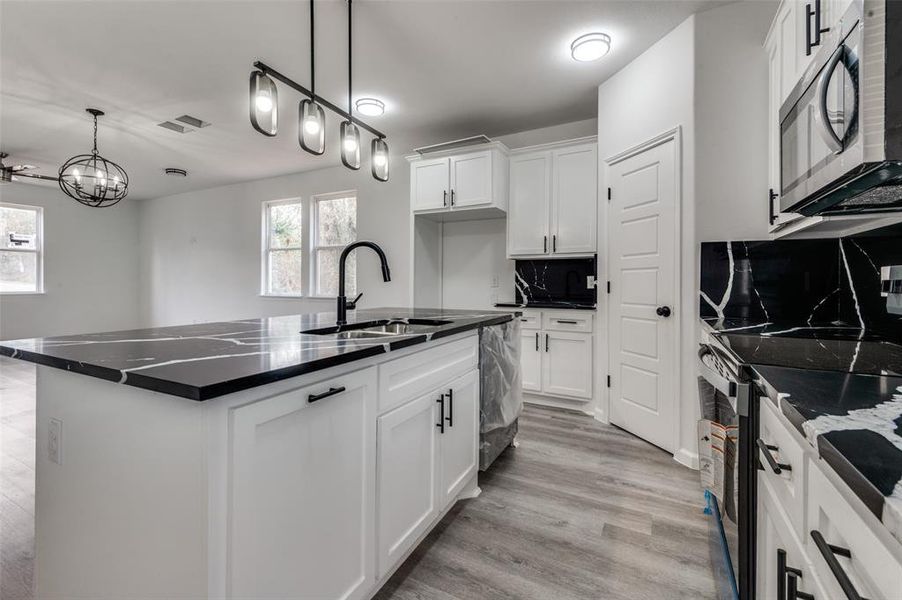 Kitchen featuring a kitchen island with sink, sink, light wood-type flooring, white cabinetry, and stainless steel appliances