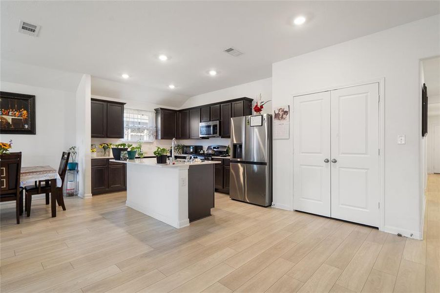 Kitchen featuring stainless steel appliances, an island with sink, recessed lighting, dark brown cabinetry, and light wood finished floors