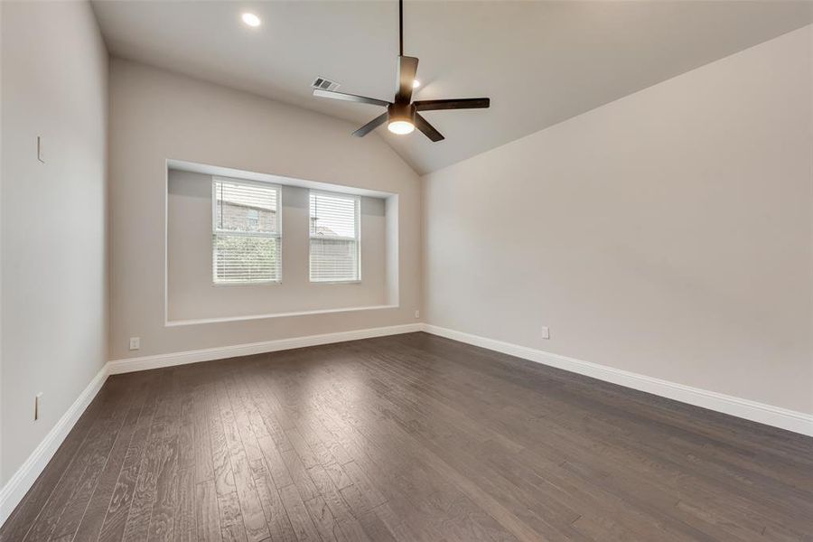 Empty room featuring dark wood-style floors, vaulted ceiling, and ceiling fan Empty room featuring dark wood-style floors, vaulted ceiling, and ceiling fan