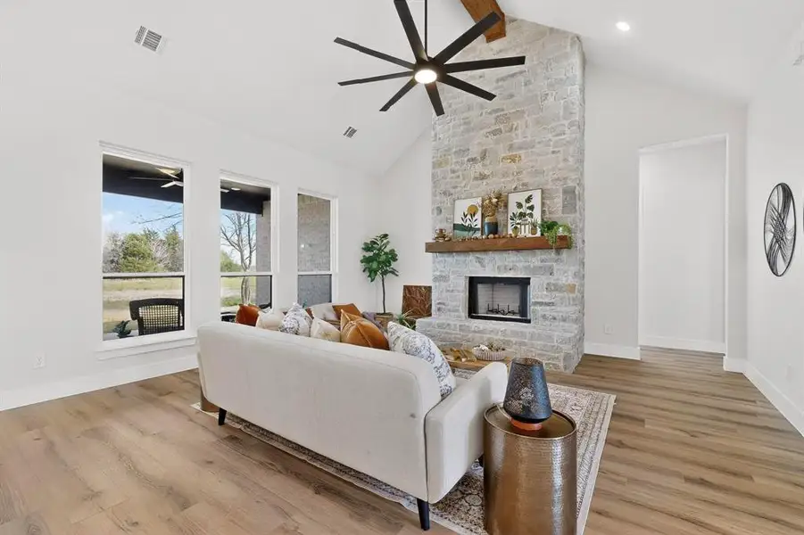 Living area with a ceiling fan, light wood-type flooring, and a stone fireplace
