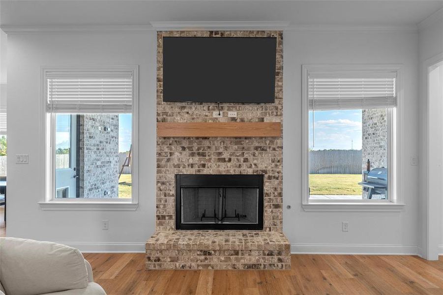 Living room featuring a brick fireplace, ornamental molding, and wood finished floors Living room featuring a brick fireplace, ornamental molding, and wood finished floors