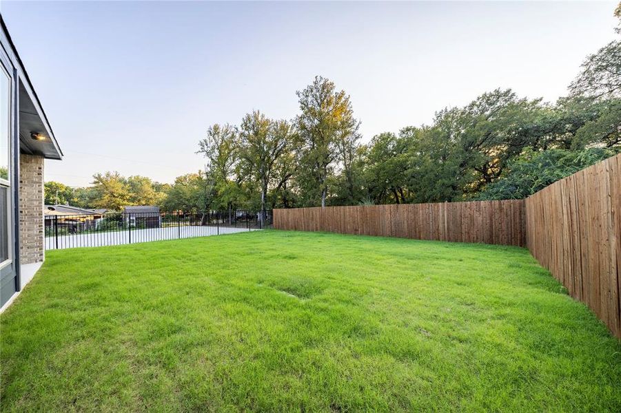 Fenced backyard with view of wooded area