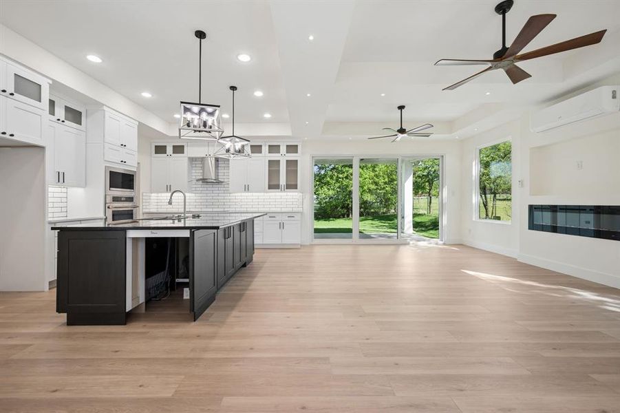 Kitchen featuring glass fronted cabinets, a center island with sink, open floor plan, backsplash, and a raised ceiling