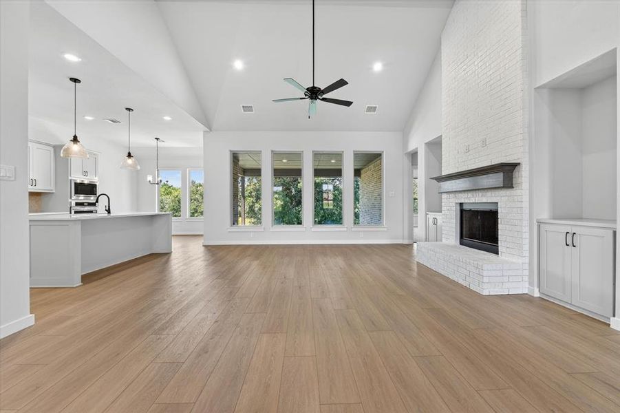 Spacious interior featuring wood-finish flooring, a vaulted ceiling, and a fireplace with a white brick surround and dark mantel