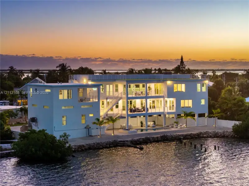 Waterfront multi-story residence featuring tiered balconies, a rooftop deck, exterior staircase, and a ground-level swimming pool Waterfront multi-story residence featuring tiered balconies, a rooftop deck, exterior staircase, and a ground-level swimming pool
