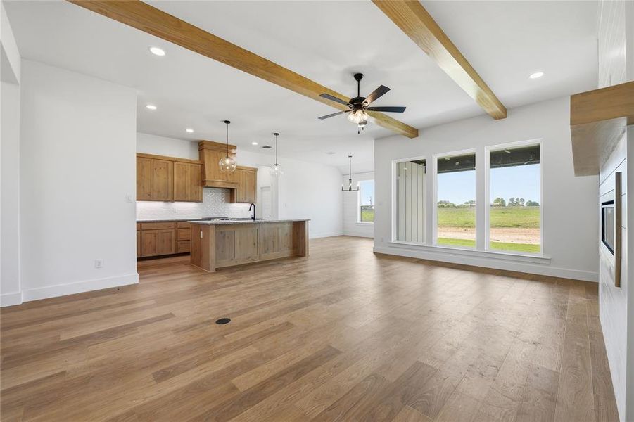 Unfurnished living room featuring ceiling fan, hanging lights, light wood-style floors, beam ceiling, and a fireplace Unfurnished living room featuring ceiling fan, hanging lights, light wood-style floors, beam ceiling, and a fireplace