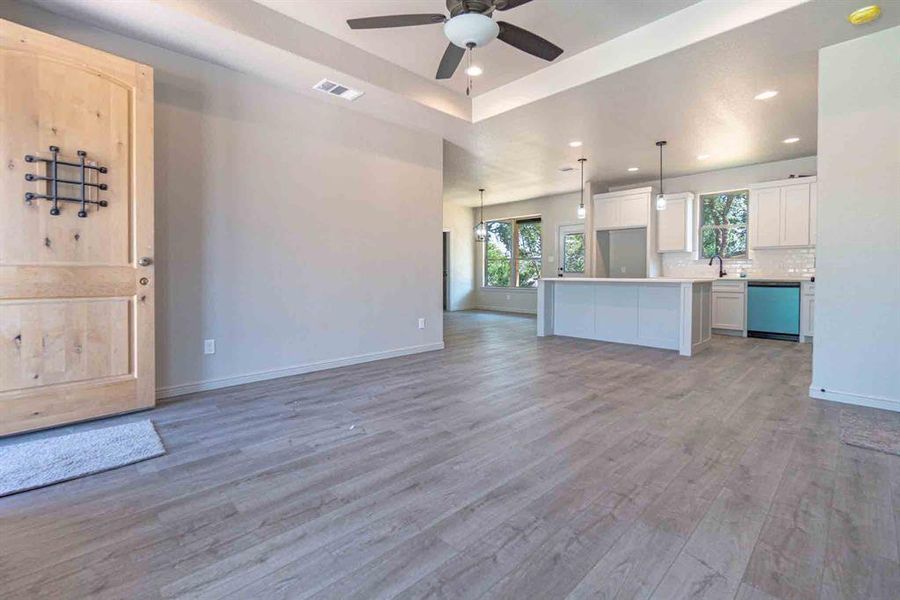 Unfurnished living room featuring dark wood-style floors, recessed lighting, a raised ceiling, and ceiling fan