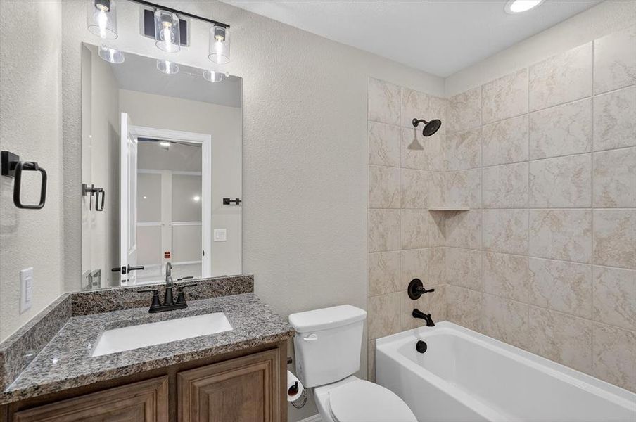 Bathroom featuring a bathtub with tiled surround, a built-in shower shelf, a vanity with a granite countertop, and dark wood-finish cabinetry Bathroom featuring a bathtub with tiled surround, a built-in shower shelf, a vanity with a granite countertop, and dark wood-finish cabinetry