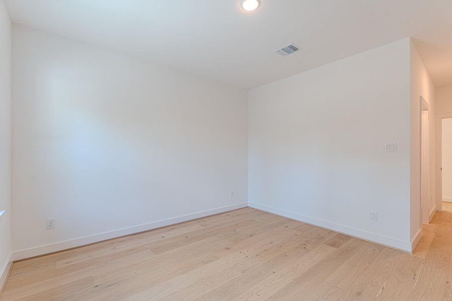 Bright, spacious room with light wood flooring, white walls, and recessed lighting. Ideal for a bedroom or office.