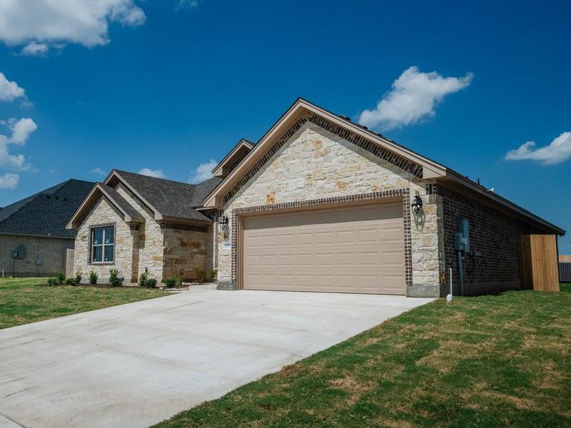 View of front of home featuring stone siding, a front lawn, an attached garage, and driveway View of front of home featuring stone siding, a front lawn, an attached garage, and driveway