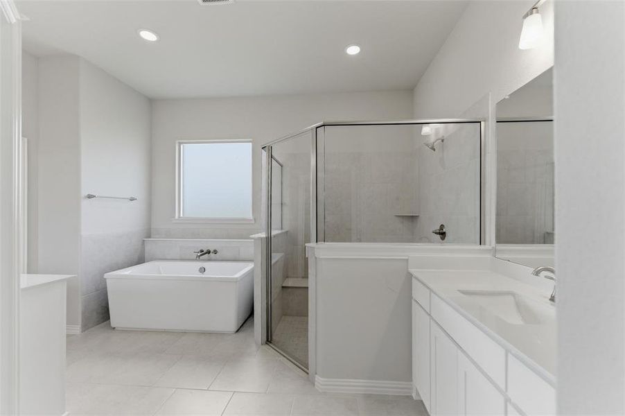 Bathroom featuring a freestanding tub, a glass-enclosed shower, dual vanity with a white countertop, and light-colored tile flooring