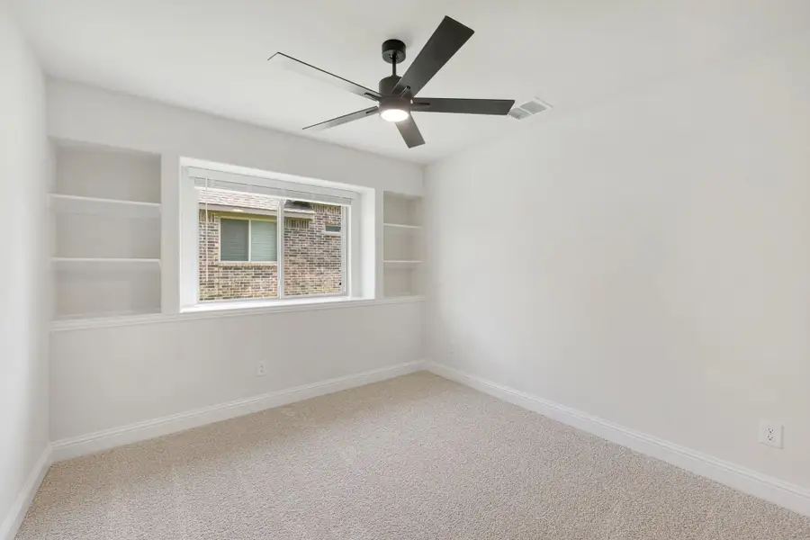 Empty bedroom with built-in shelves, ceiling fan, carpet flooring, and a window with natural light