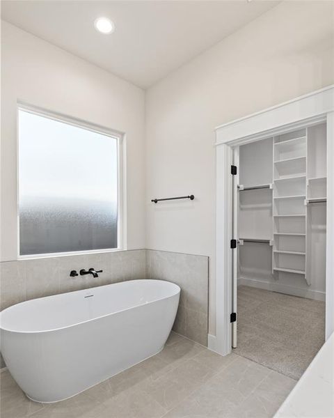 Bathroom with a walk in closet, tile walls, recessed lighting, a freestanding tub, and wainscoting