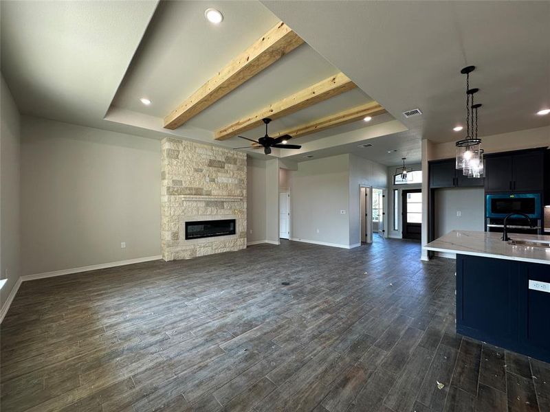 Unfurnished living room featuring beam ceiling, recessed lighting, a stone fireplace, ceiling fan, and dark wood-type flooring Unfurnished living room featuring beam ceiling, recessed lighting, a stone fireplace, ceiling fan, and dark wood-type flooring