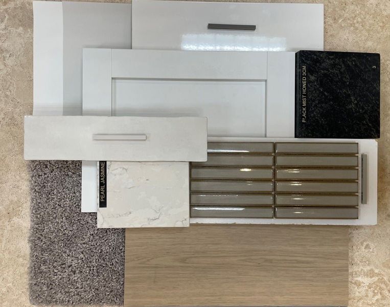 Home design material samples including white cabinet doors, Pearl Jasmine quartz, Black Mist granite, tan tile, carpet, and wood flooring.