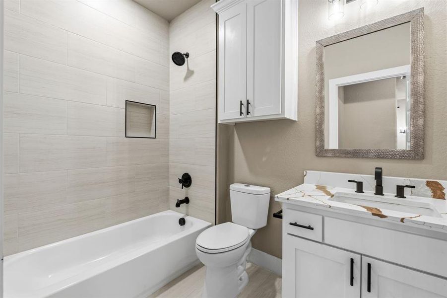 Full Bathroom upstairs featuring a white vanity with a patterned countertop, a built-in tub with tile surround, black plumbing fixtures, and white cabinetry